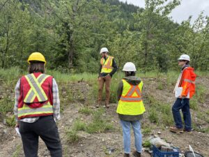 Workers in high visibility vests and hard hats attending staff training in an open field with forest behind.