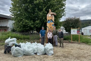 Three volunteers stand with CSISS staff in front of Splatsin garden at Belvidere Park in Enderby.