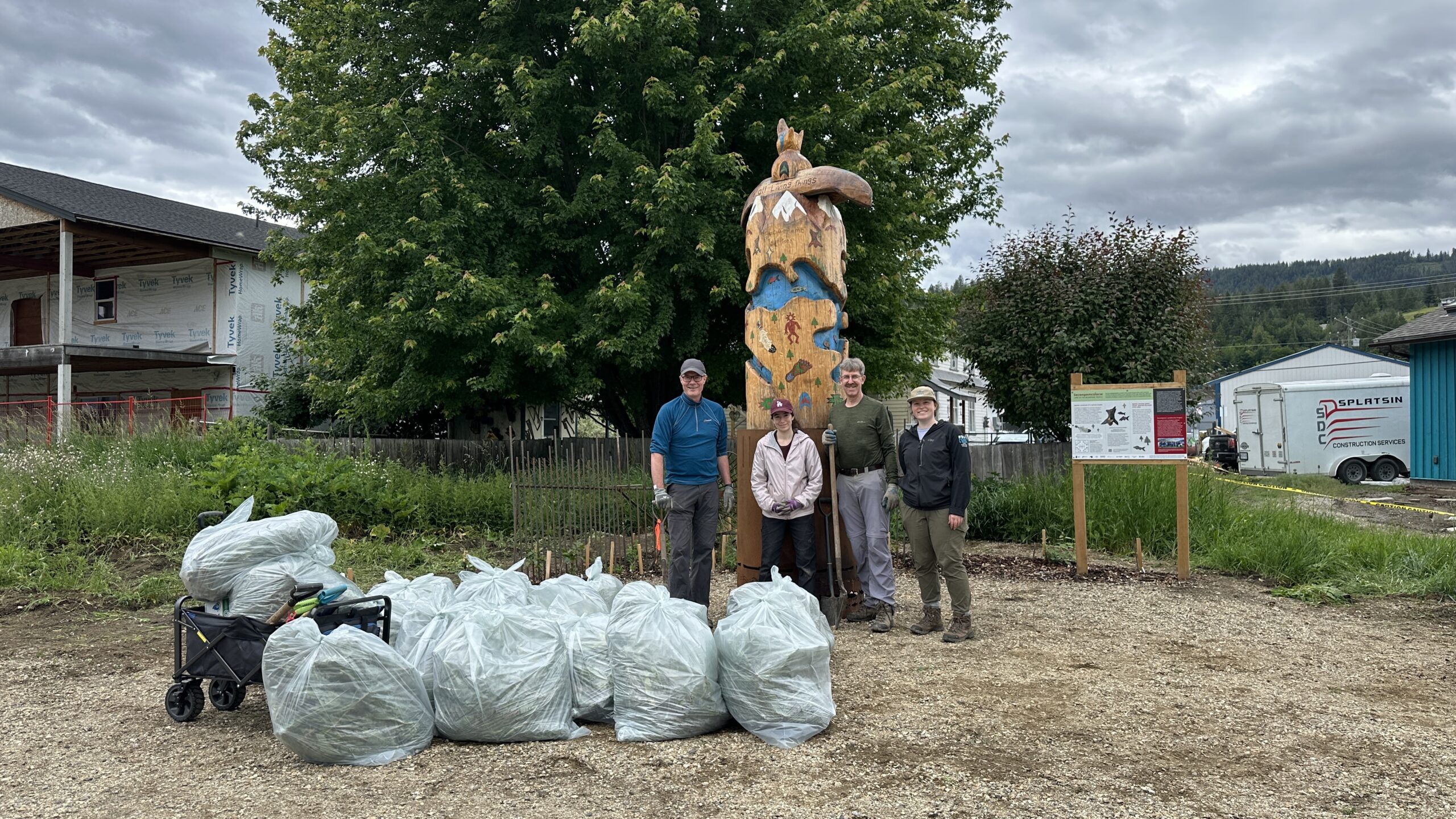 Three volunteers stand with CSISS staff in front of Splatsin garden at Belvidere Park in Enderby.